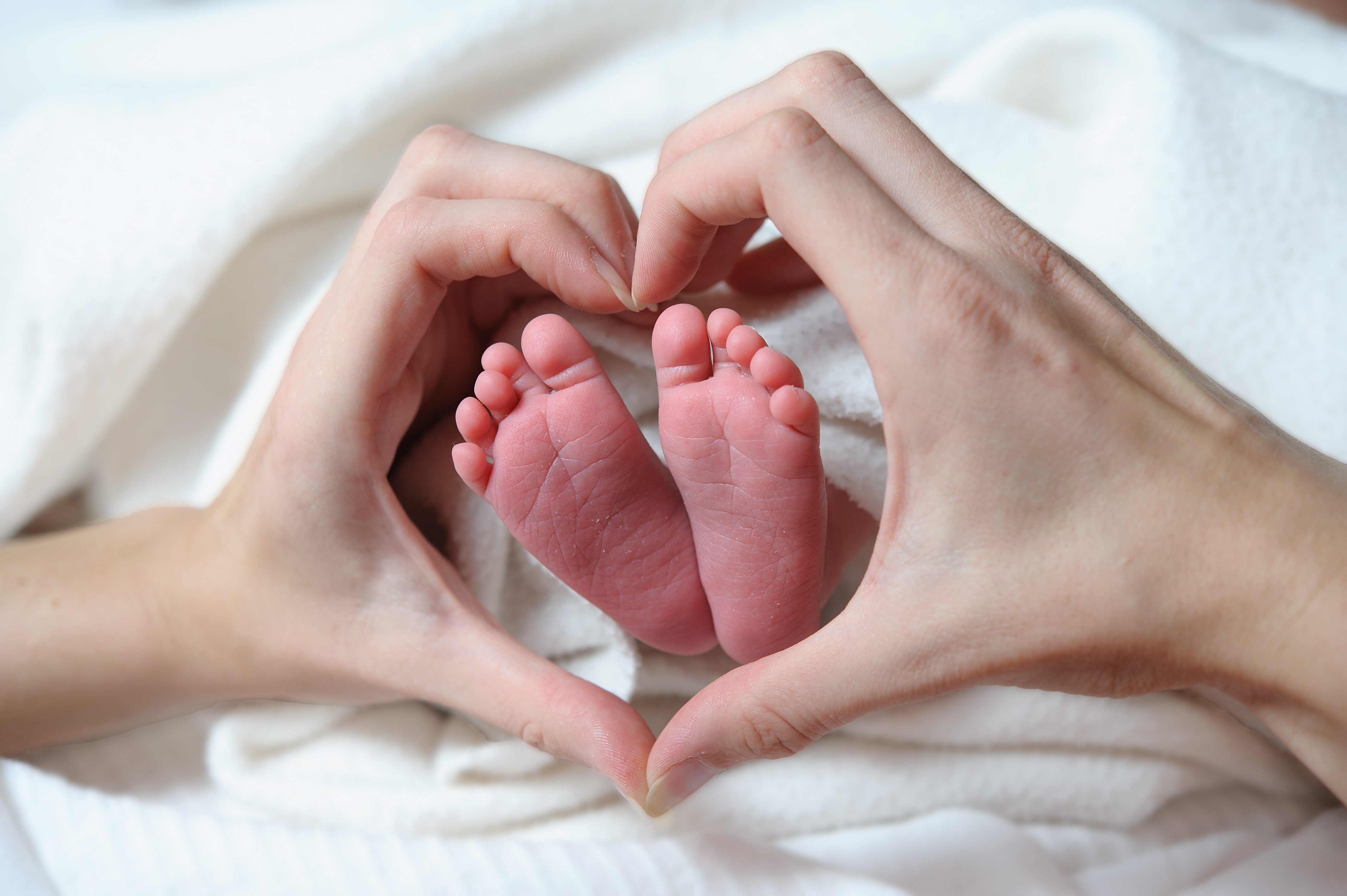 Babyfüsse in herzförmig gehaltenen Händen – Mutter & Kind Therapie